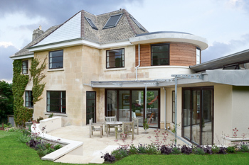 Image showing the exterior of the house from the garden.  The image shows how the terne-coated stainless steel roofing and curved timber boarding juxtapose the local Bath stone ashlar, render and clay roof tiles.