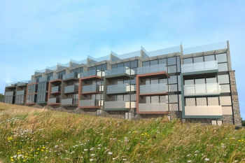Image showing the cliff side exterior of the contemporary development designed by Hetreed Ross.  The images shows how the low maintenance materials such as zinc, natural stone and acetylated timber create a harmony between the scheme and the surrounding environment.