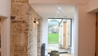 View allow internal corridor with bath stone and plastered walls and large window at end looking onto garden