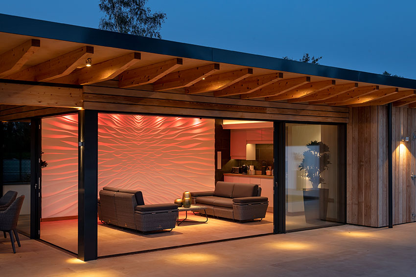 Night image of the poolside enclosed social area with internal multicolored lighting projected on the textured wall