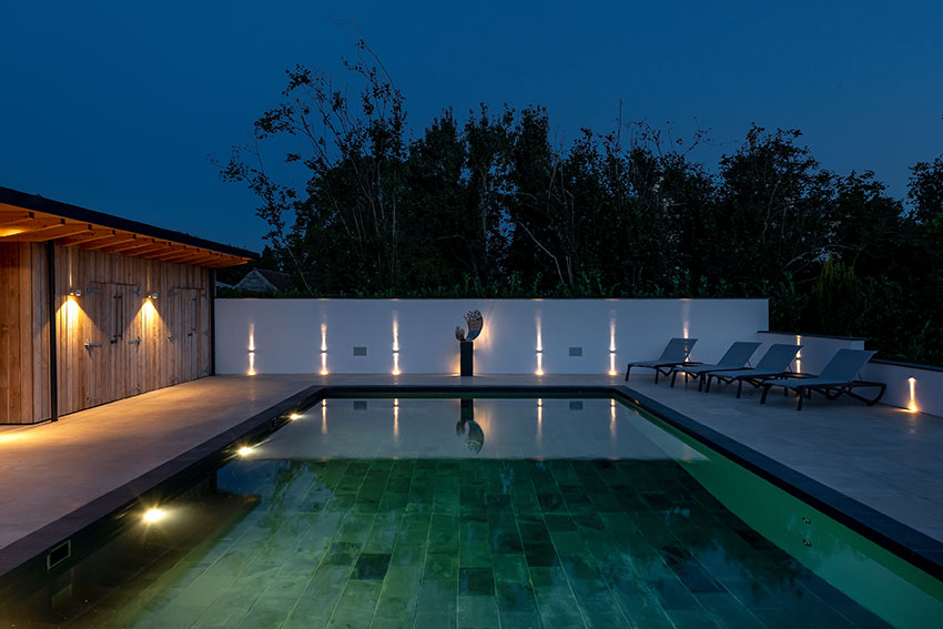 Night time image of the reflective swimming pool and outdoor contemporary art sculpture with directional lighting