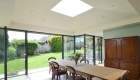 Dining room with pyramid roof form and rooflight above and full height glazing to view of garden